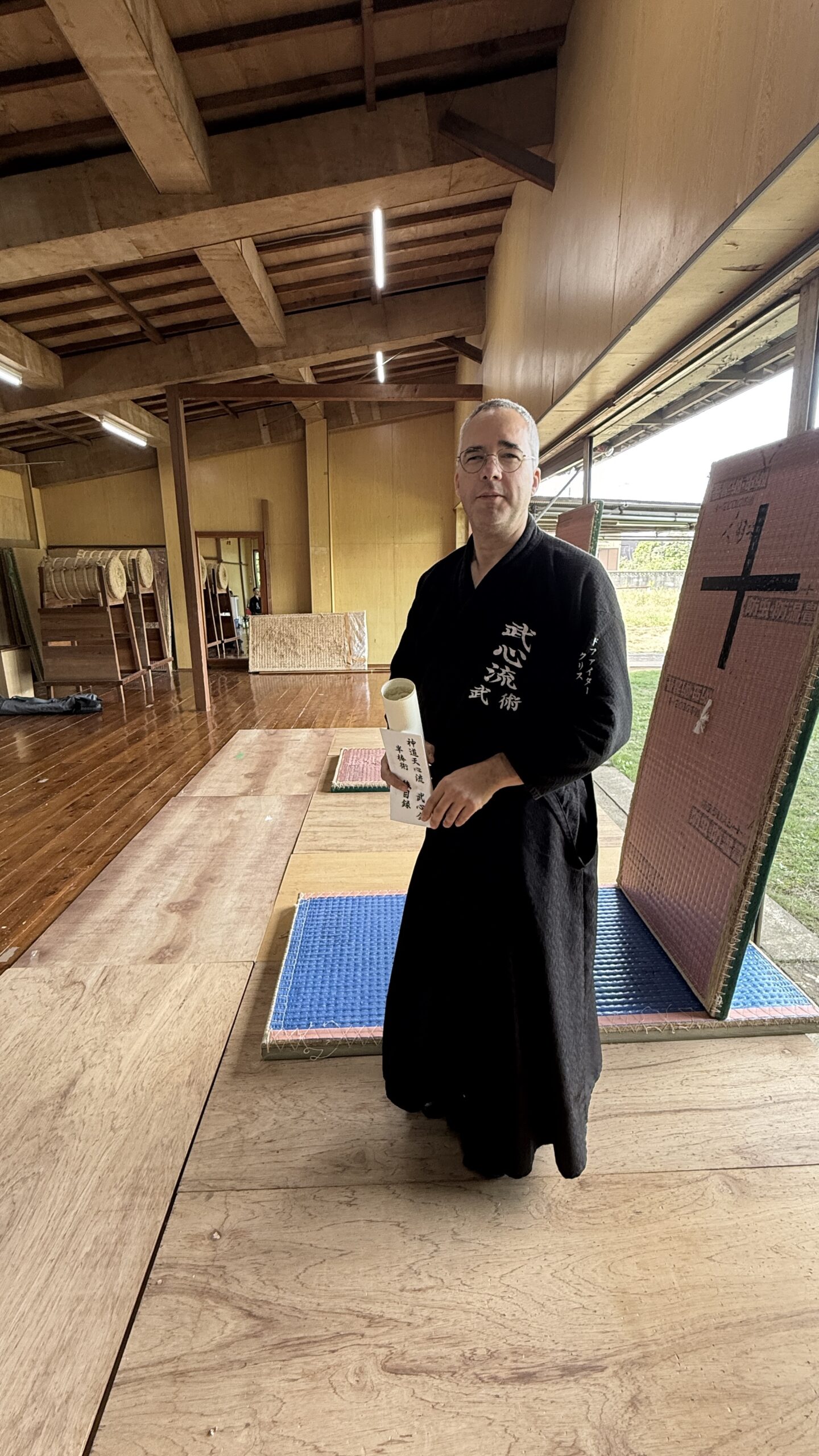 Chris de Feijter standing in a wooden dojo wearing black training clothing.
