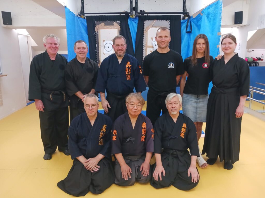 Nine Meifu Shinkage Ryū practitioners gathered in a training hall in front of practice targets.