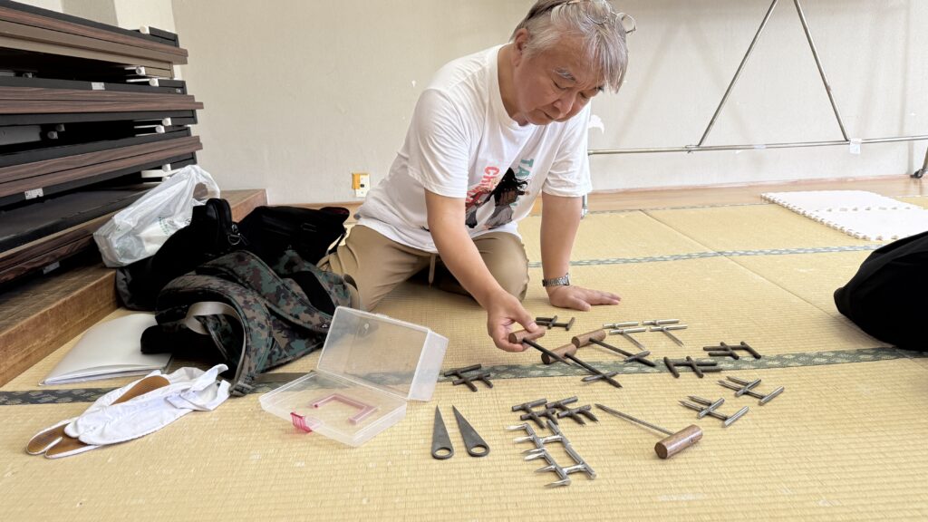A practitioner examining small handheld weapons arranged on tatami mats.