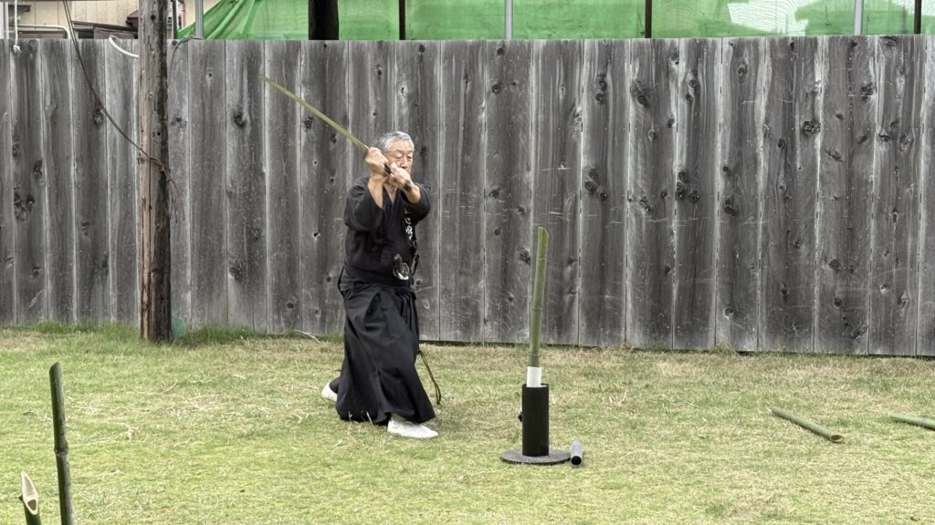 A swordsman practising outdoors beside a bamboo cutting target.
