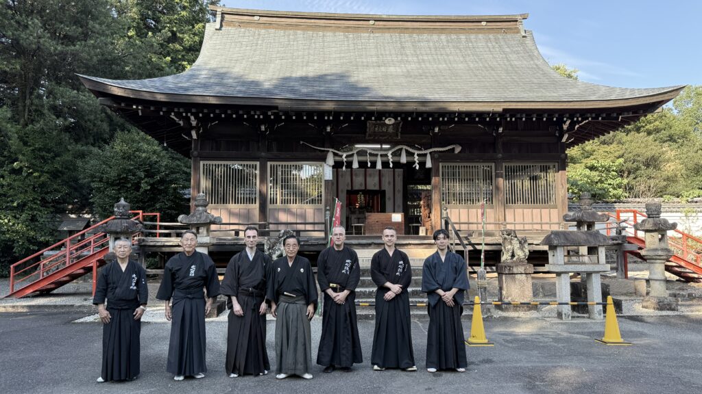 Seven martial artists gathered outside a Japanese shrine.